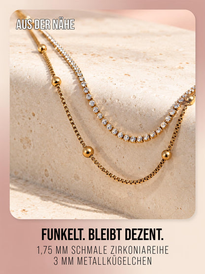 Detail der Daily Spark Halskette in Gold: Zirkoniareihe und Metallkügelchen auf hellem Stein