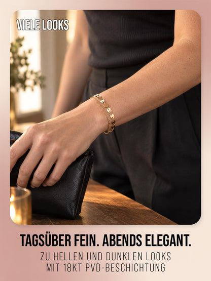 Solea Coins in Gold am Handgelenk zu schwarzer Kleidung und Tasche. Bildtext zur 18kt PVD-Beschichtung der Variante Gold.