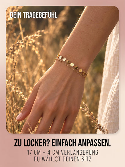 Solea Coins in Gold am Handgelenk neben Gräsern im Sonnenlicht. Bildtext: 17 cm plus 4 cm Verlängerung.